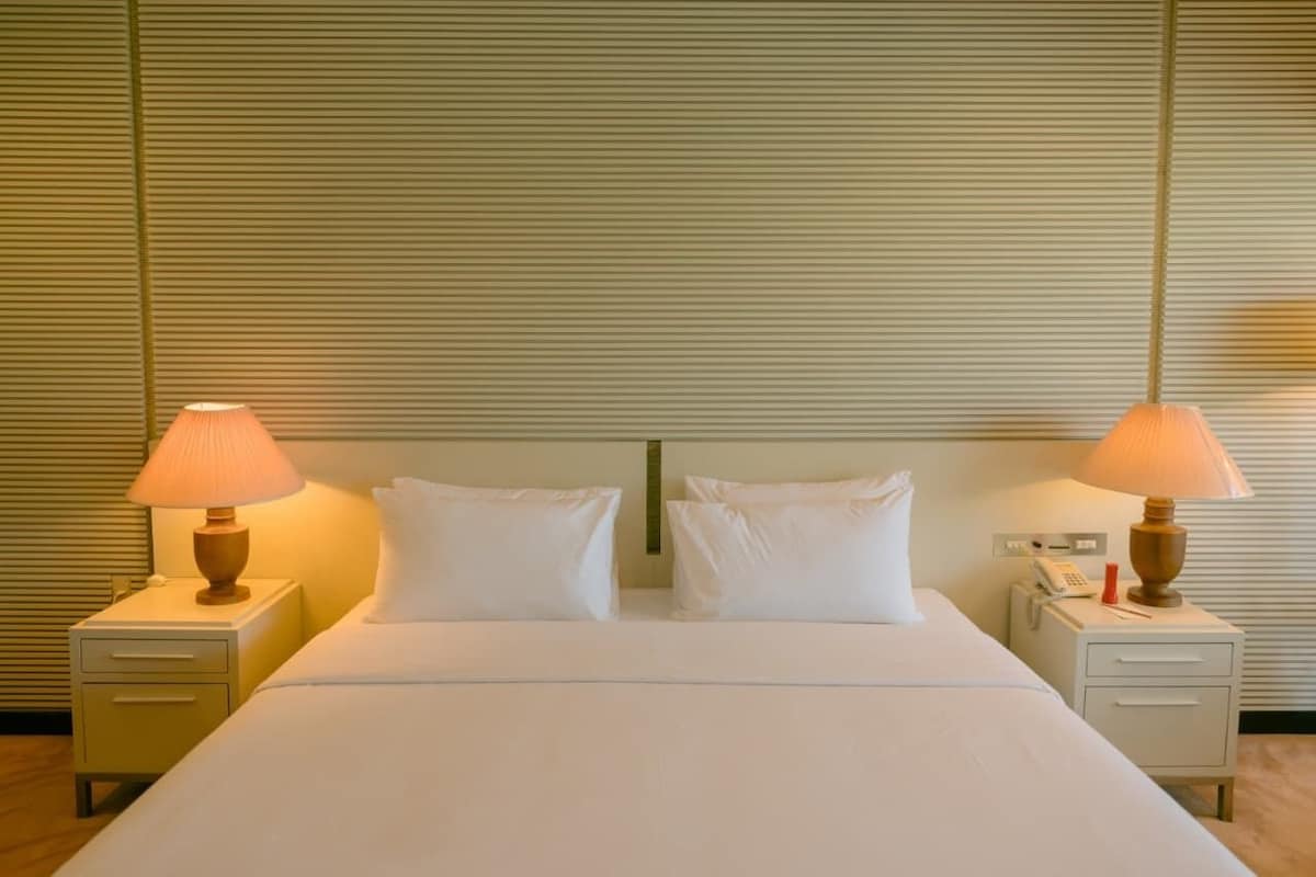 Una habitación de hotel con una cama grande, dos mesitas de noche, lámparas y un teléfono.