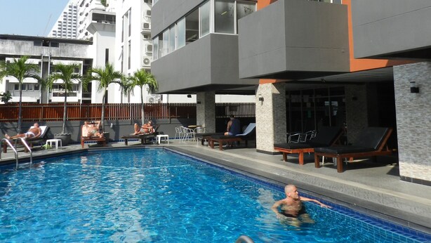 Zona de piscina con sillones de descanso y un edificio moderno con balcones.