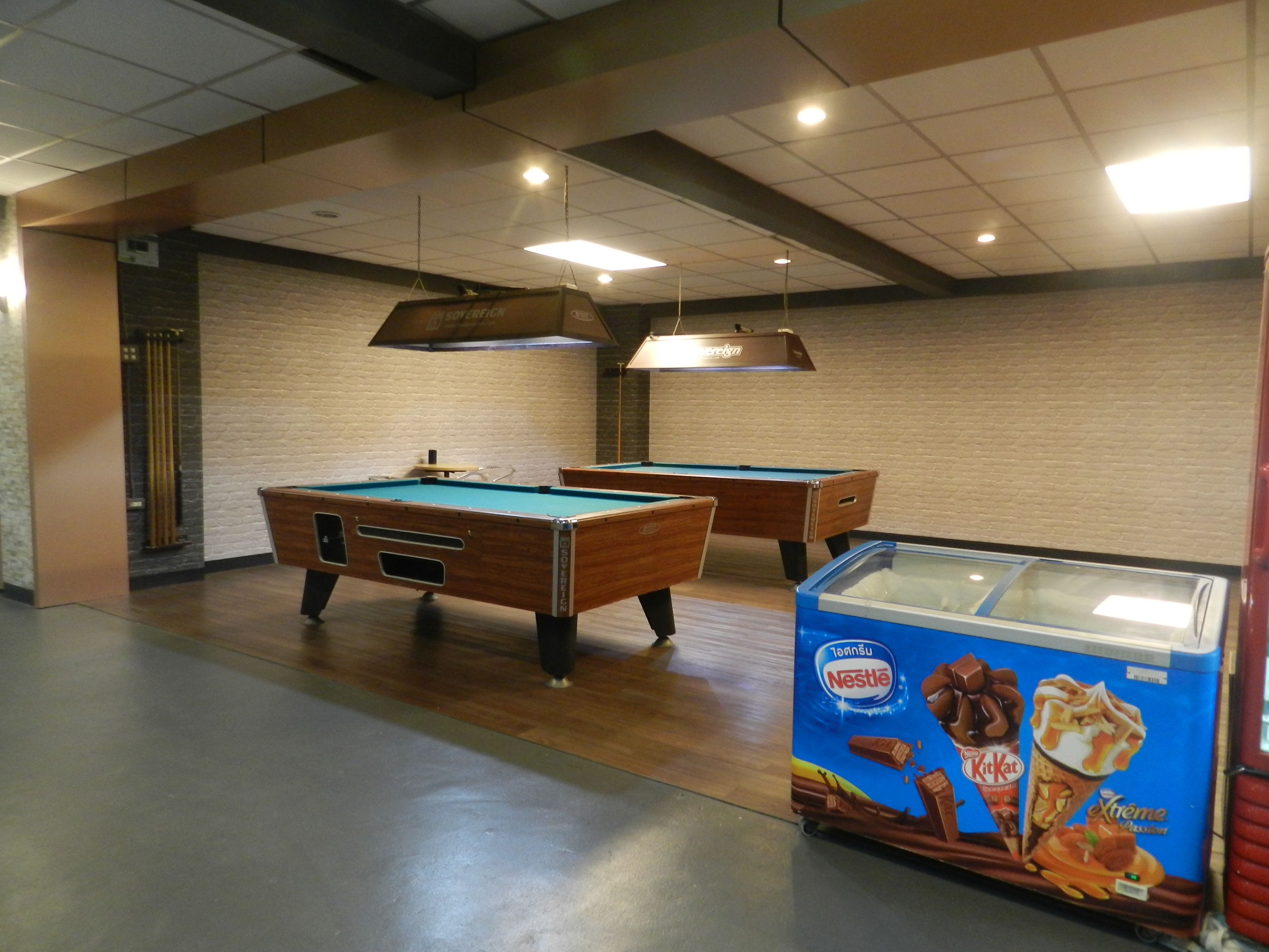 A billiards room with two pool tables, a glass display case with ice cream, and a brick wall.