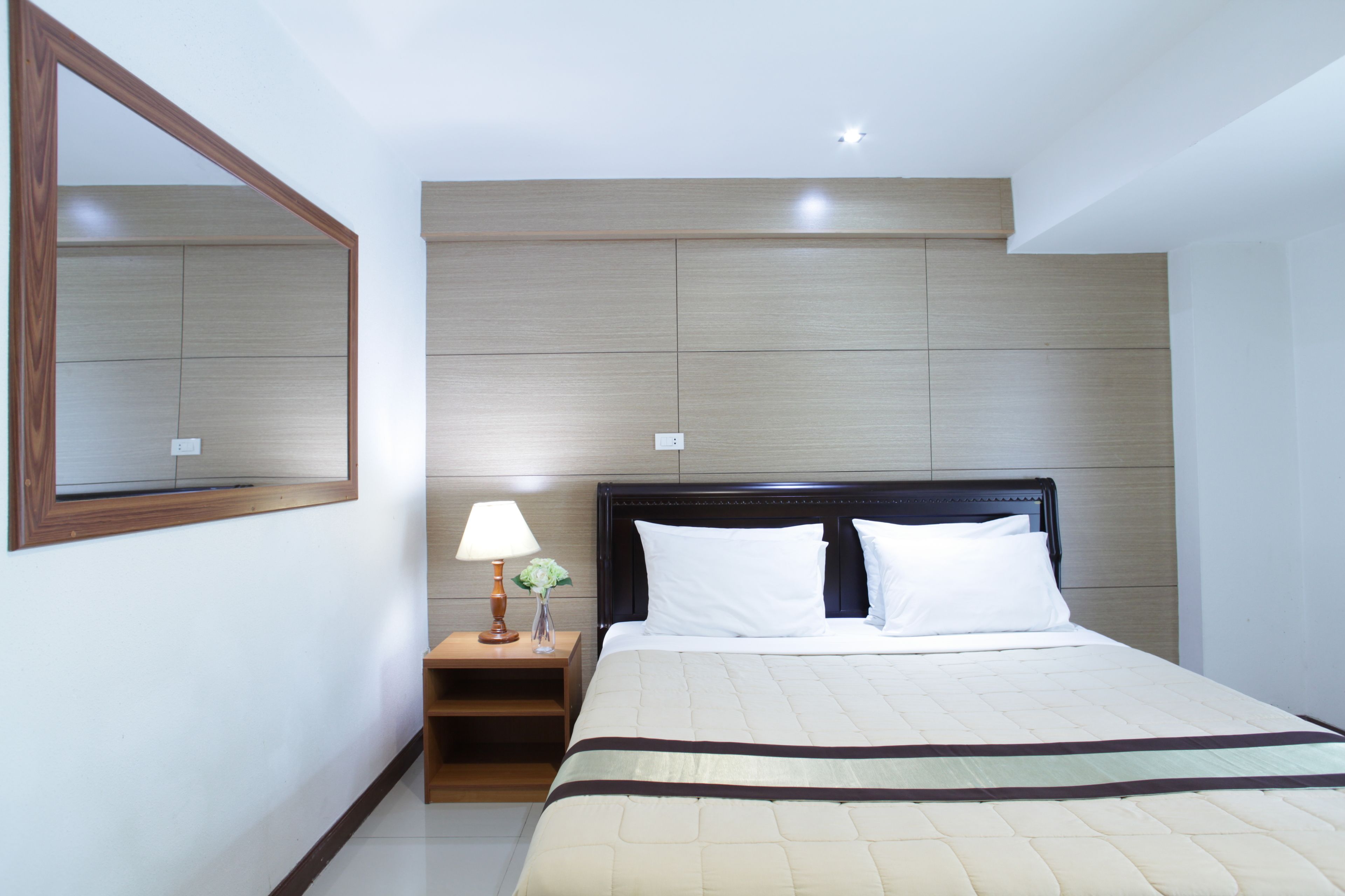 A hotel room with a large bed, a nightstand with a lamp, and a mirror on the wall.