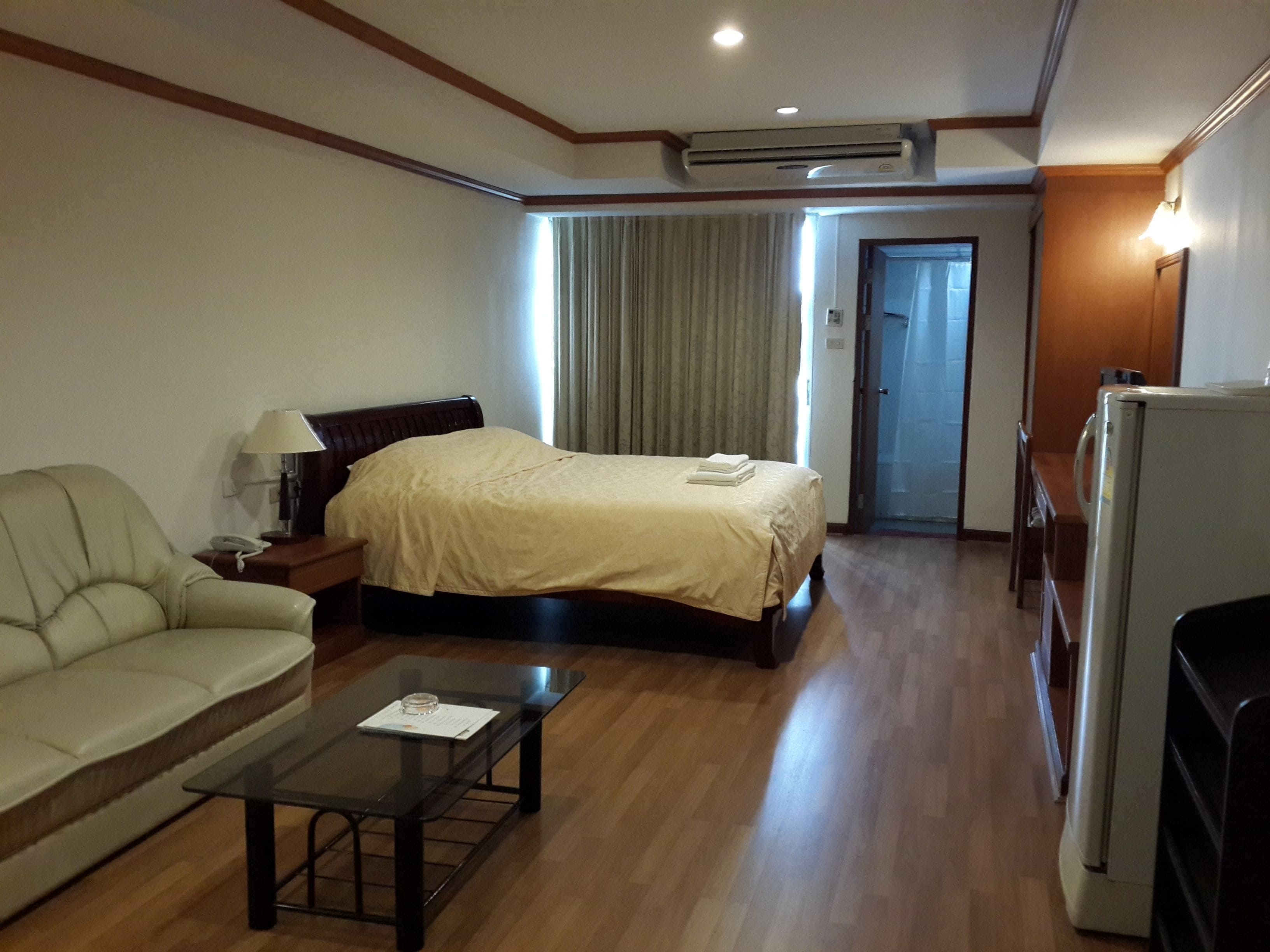 Habitación de hotel con cama, sofá, mesa de centro, aire acondicionado y refrigerador.