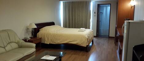 Habitación de hotel con cama, sofá, mesa de centro, aire acondicionado y refrigerador.