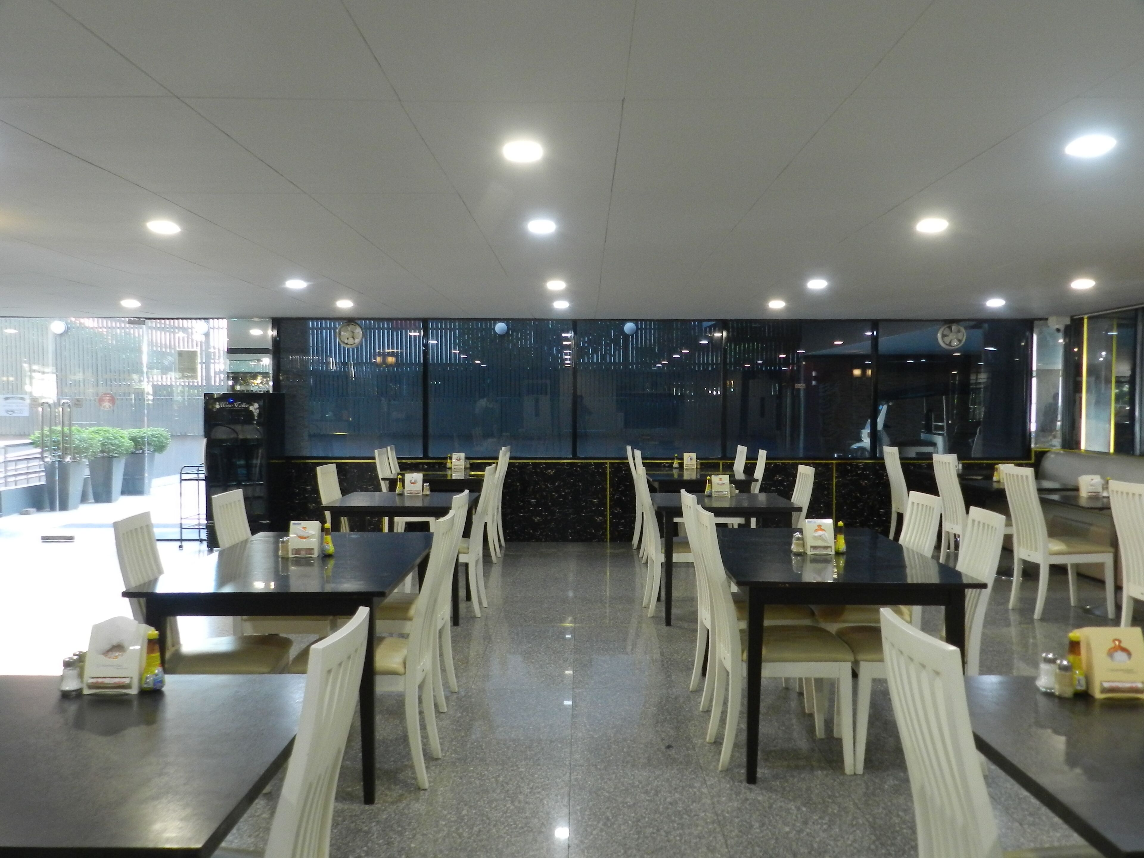 Un comedor espacioso con varias mesas y sillas, ventanas amplias que ofrecen vistas a la ciudad y un diseño de techo moderno.