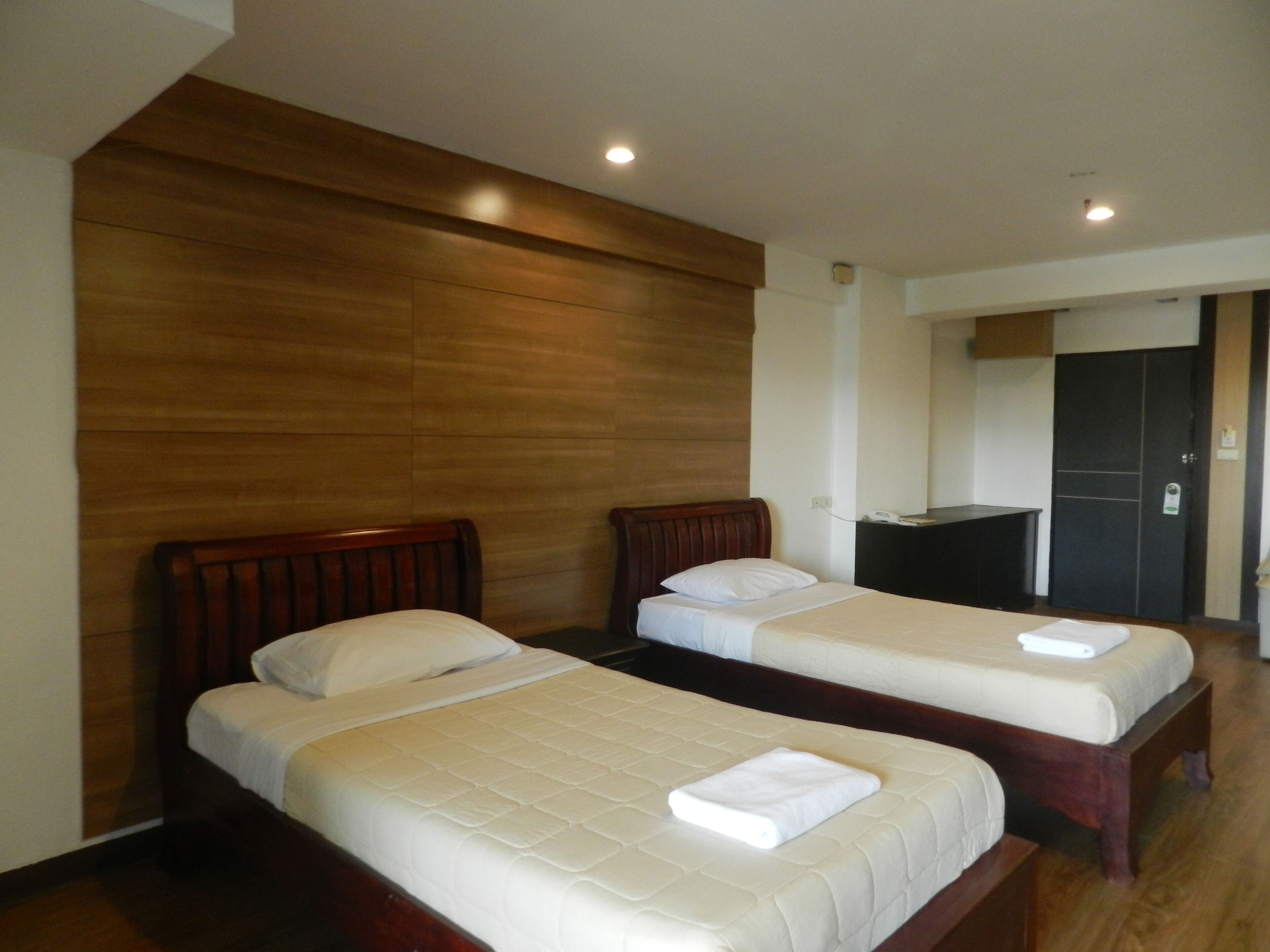A hotel room with two single beds, wooden headboards, a dark-colored desk, and a door in the background.