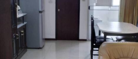 A spacious living area with a sofa, a dining table, and a kitchen area with a refrigerator and cabinets.