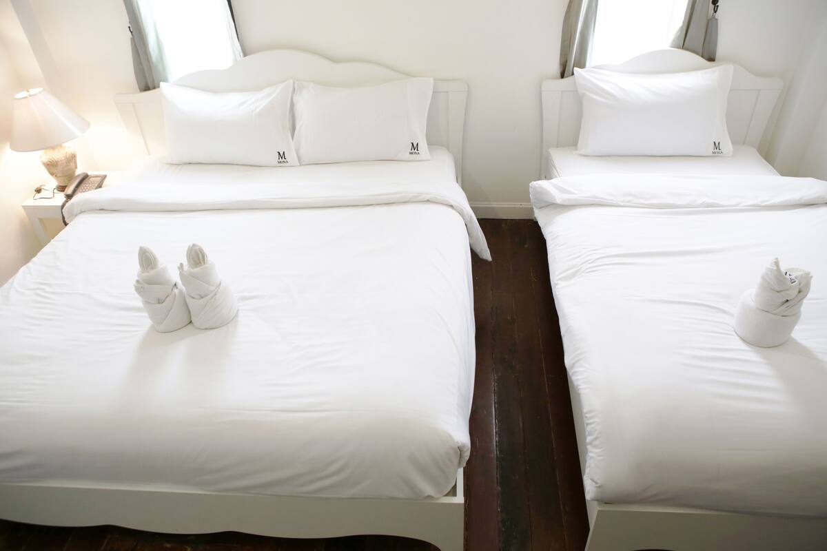 Duas camas brancas com cabeceiras e peseiras iguais, cada uma com uma almofada e uma toalha colocadas sobre a cama.