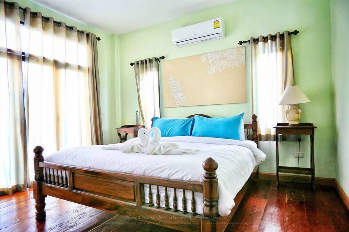 Quarto com cama de madeira, roupa de cama branca, almofadas azuis, ar condicionado fixado na parede e abajur.