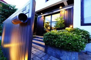 A building entrance with a metal structure, steps leading up to a door, and a planter with green foliage.