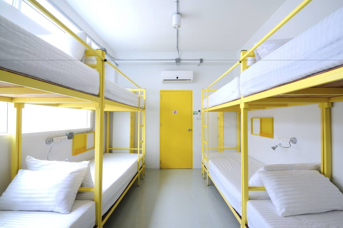 Een slaapzaal met stapelbedden, een gele deur, een airconditioning en een kleine spiegel aan de muur.