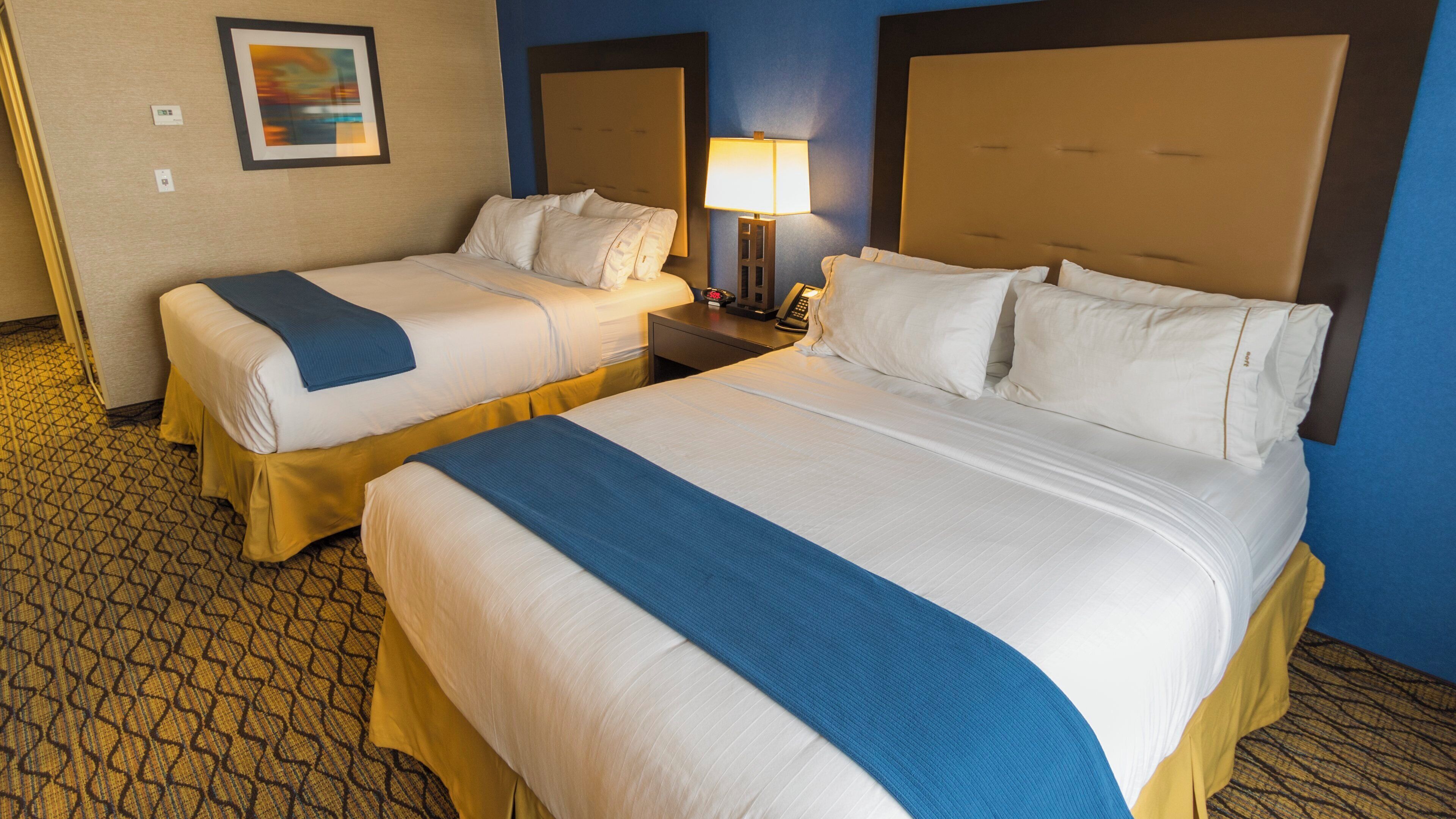 A hotel room with two beds, a nightstand with a lamp, and a painting on the wall.