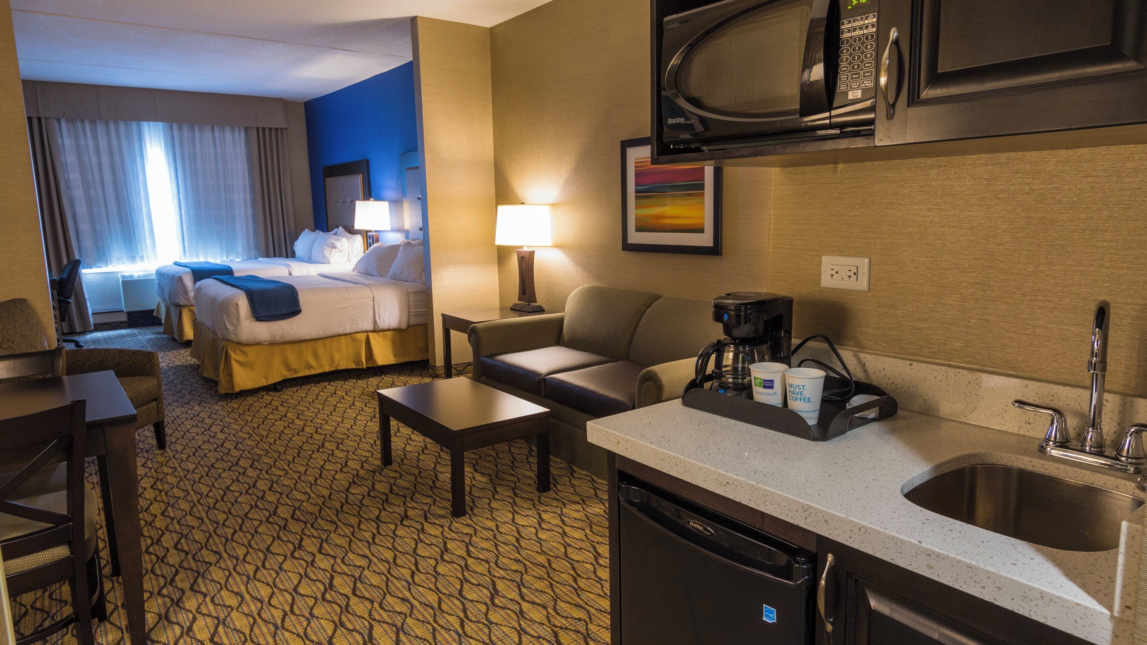 A hotel room with a bed, a sofa, a coffee maker, a microwave, and a sink.