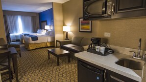 A hotel room with a bed, a desk, a chair, a coffee maker, a microwave, and a sink.