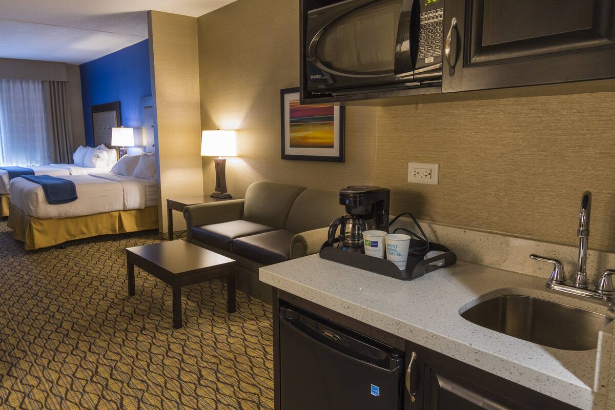 A hotel room with a bed, a desk, a chair, a coffee maker, a microwave, and a sink.