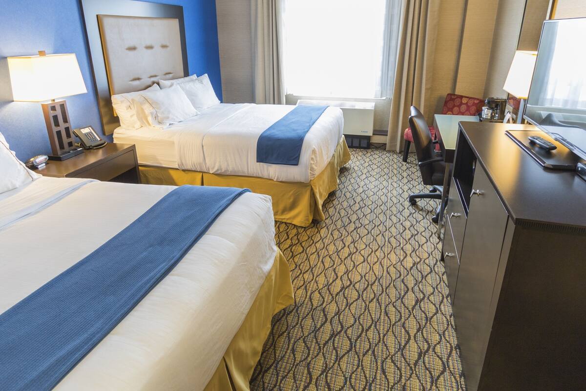 A hotel room with two beds, a desk, a television, and a window with curtains.