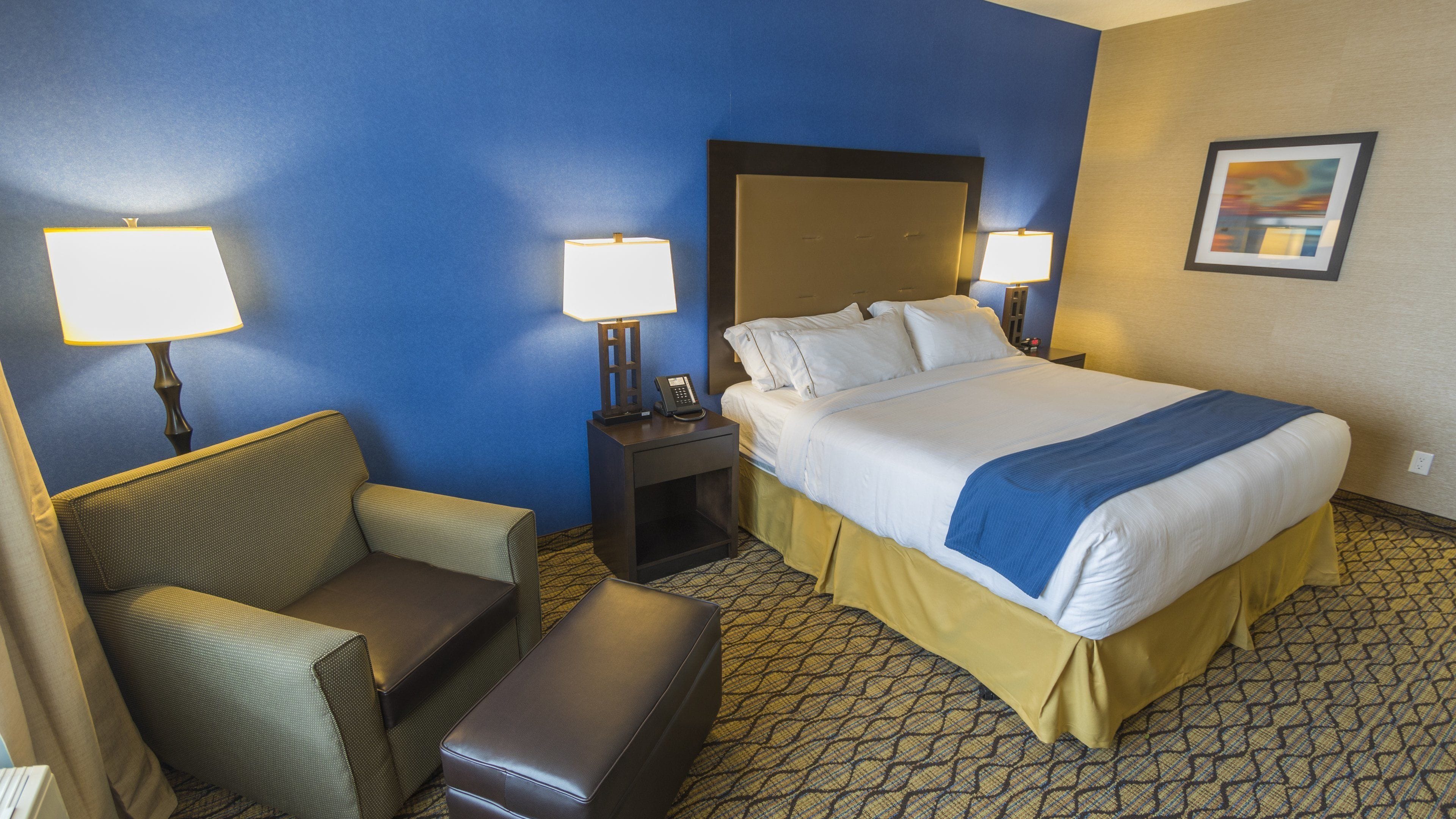 A hotel room with a bed, two bedside lamps, a chair, and a small table.