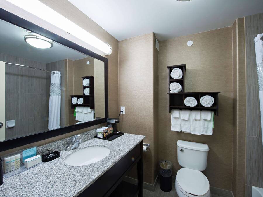 Un baño moderno con un lavabo de granito, un espejo grande, un inodoro y una cortina de ducha.