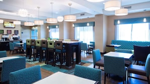 A hotel lobby with a bar area, seating arrangements, and a television screen. - Hampton Inn Saskatoon South (Saskatoon)