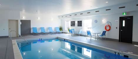 An indoor swimming pool with clear water, marked depth lines, and a lifebuoy on the wall.