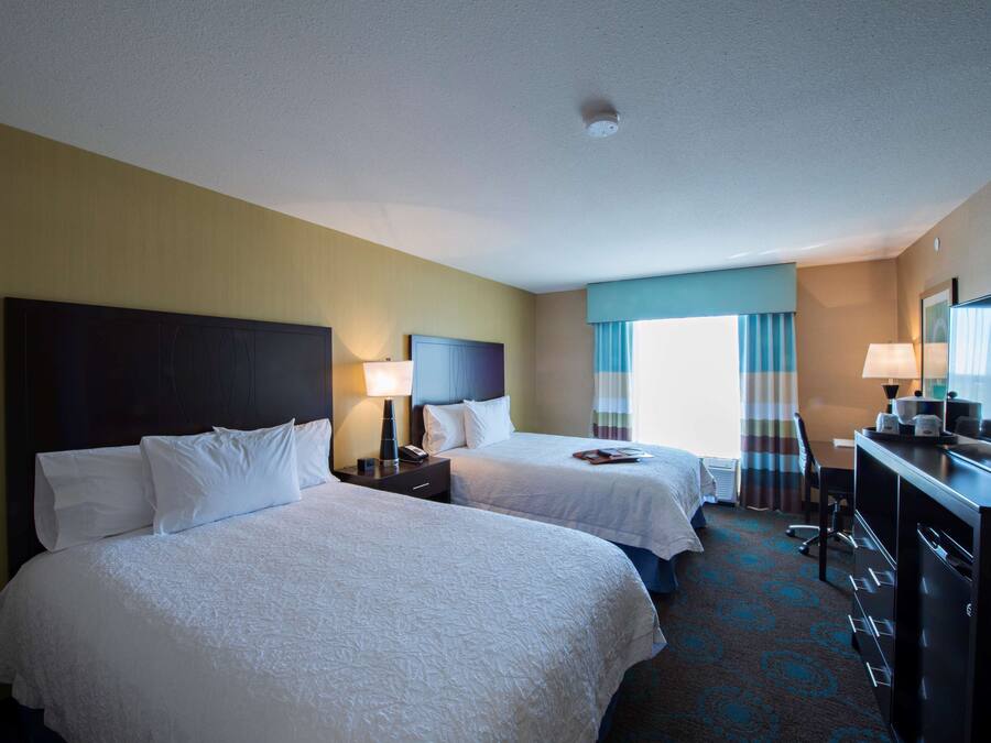 A hotel room with two beds, a desk, a chair, and a dresser.