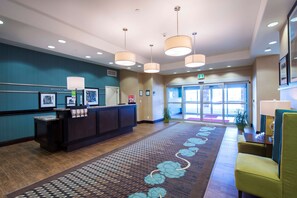 A reception area with a reception desk, framed pictures, a patterned carpet, and a green chair.
