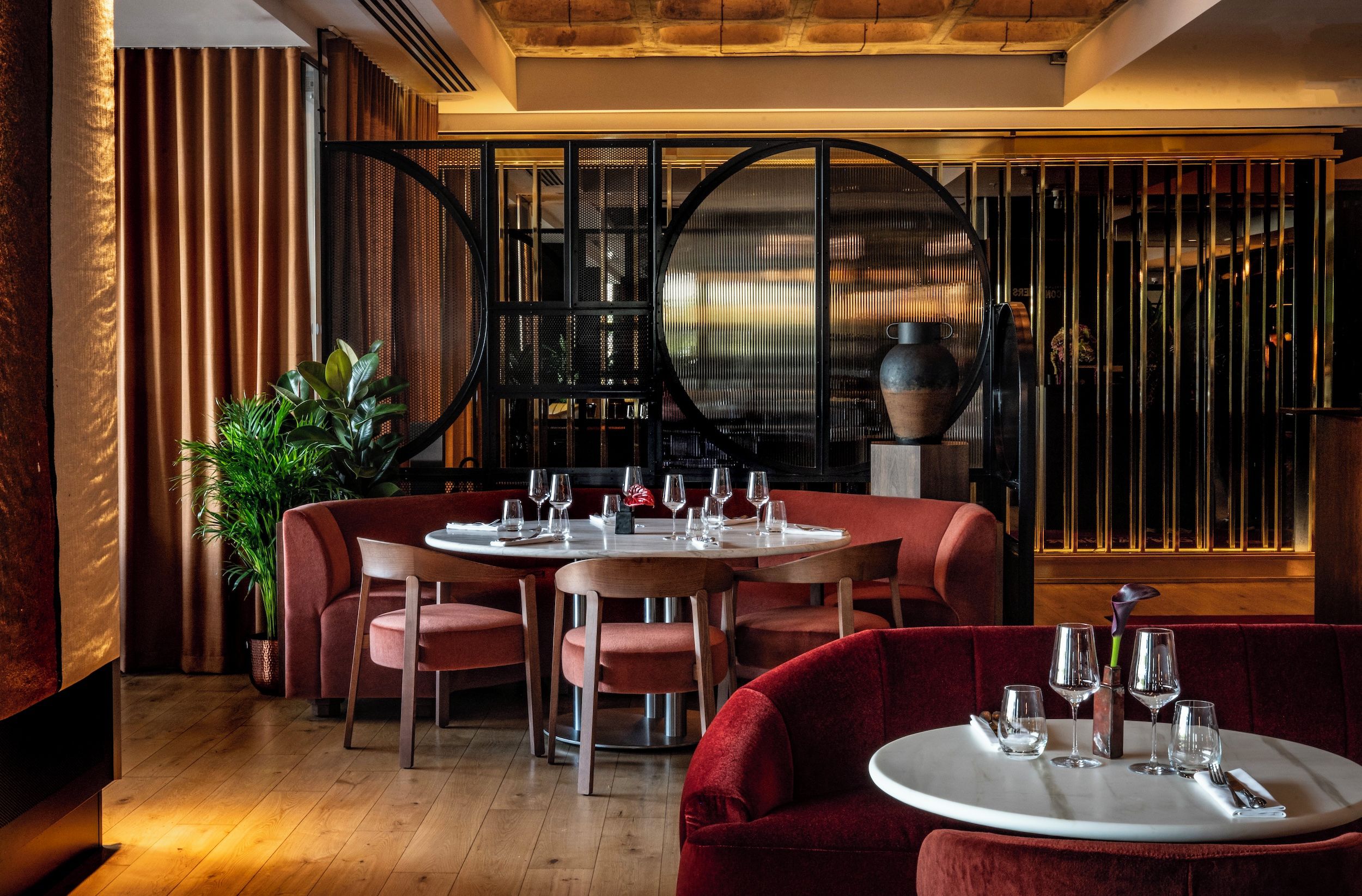 A restaurant interior with a round table, red upholstered chairs, and a bar area with a circular mirror.