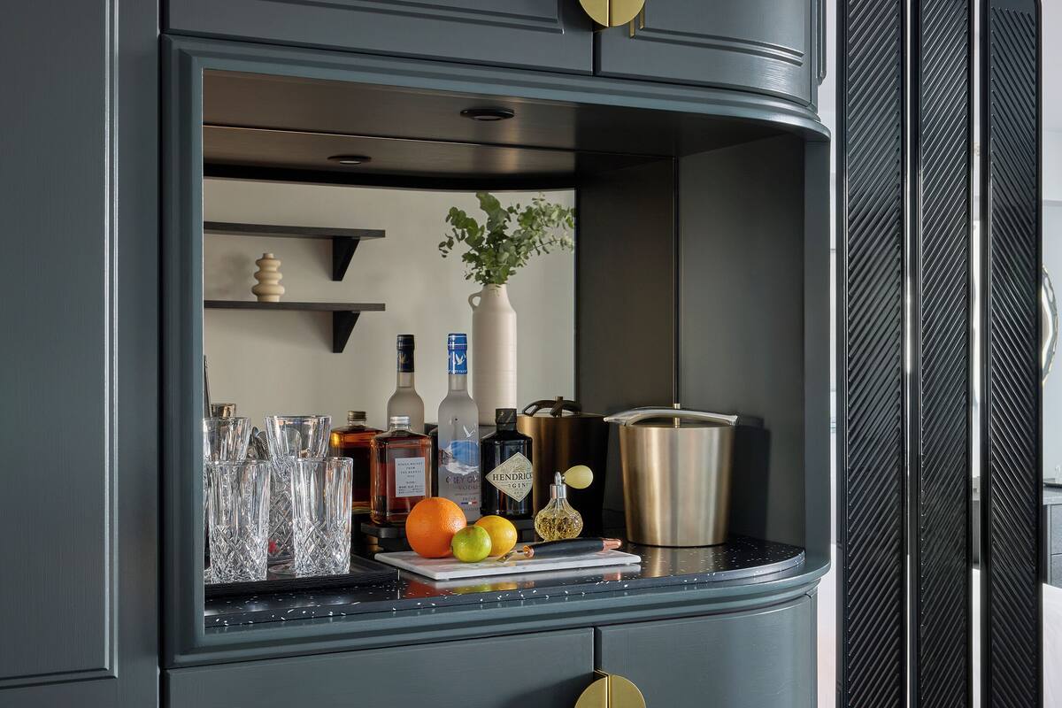 A bar area with a counter, bottles, glasses, fruits, and a vase.