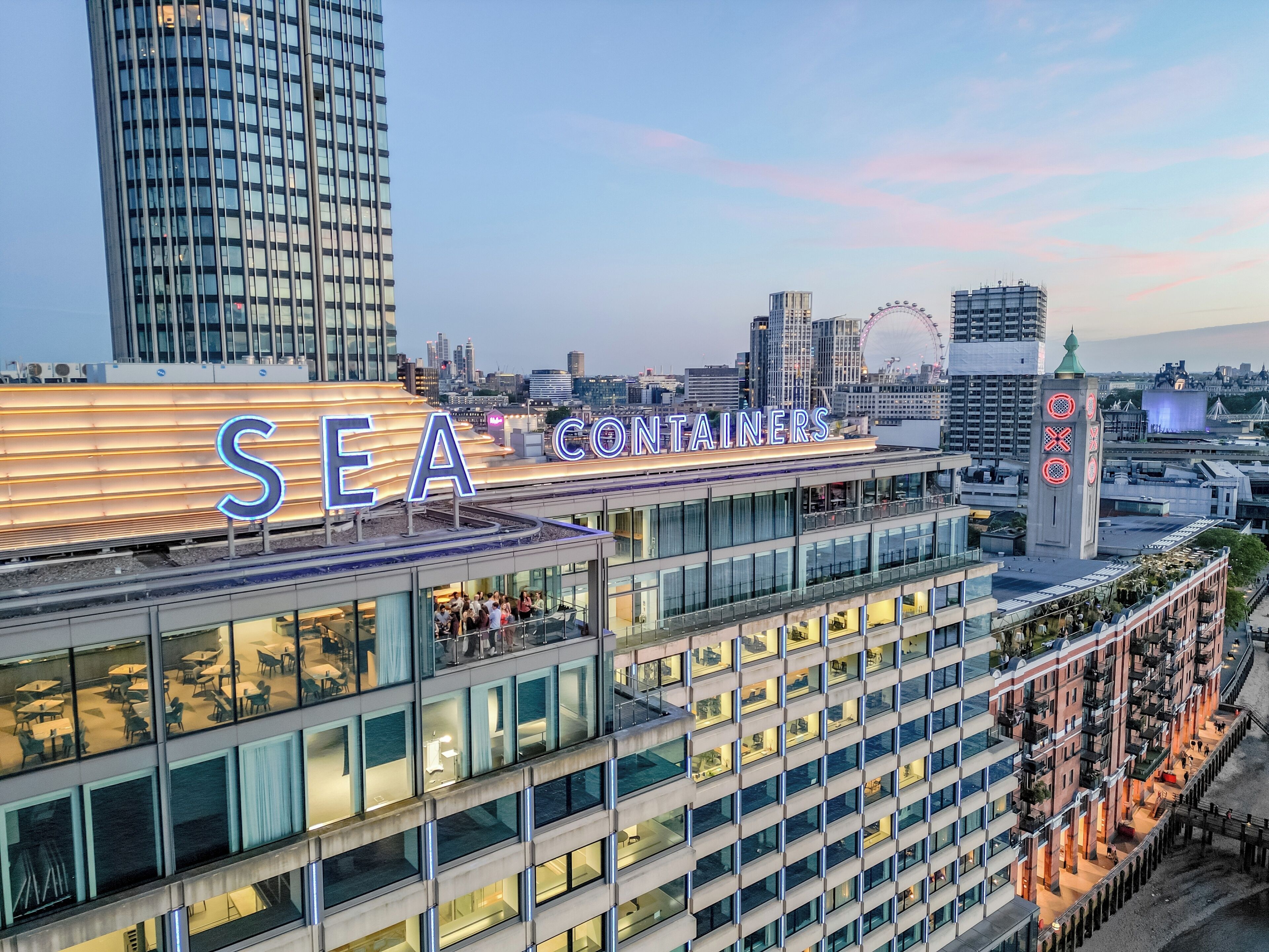 A modern hotel with a prominent 'SEA CONTAINERS' sign, multiple floors with balconies, and a city skyline in the background.