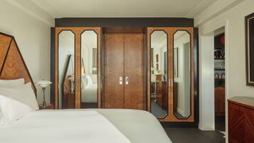 Quarto de hotel com uma cama grande, um guarda-roupa com portas espelhadas, uma mesa de cabeceira com abajur e uma cômoda.