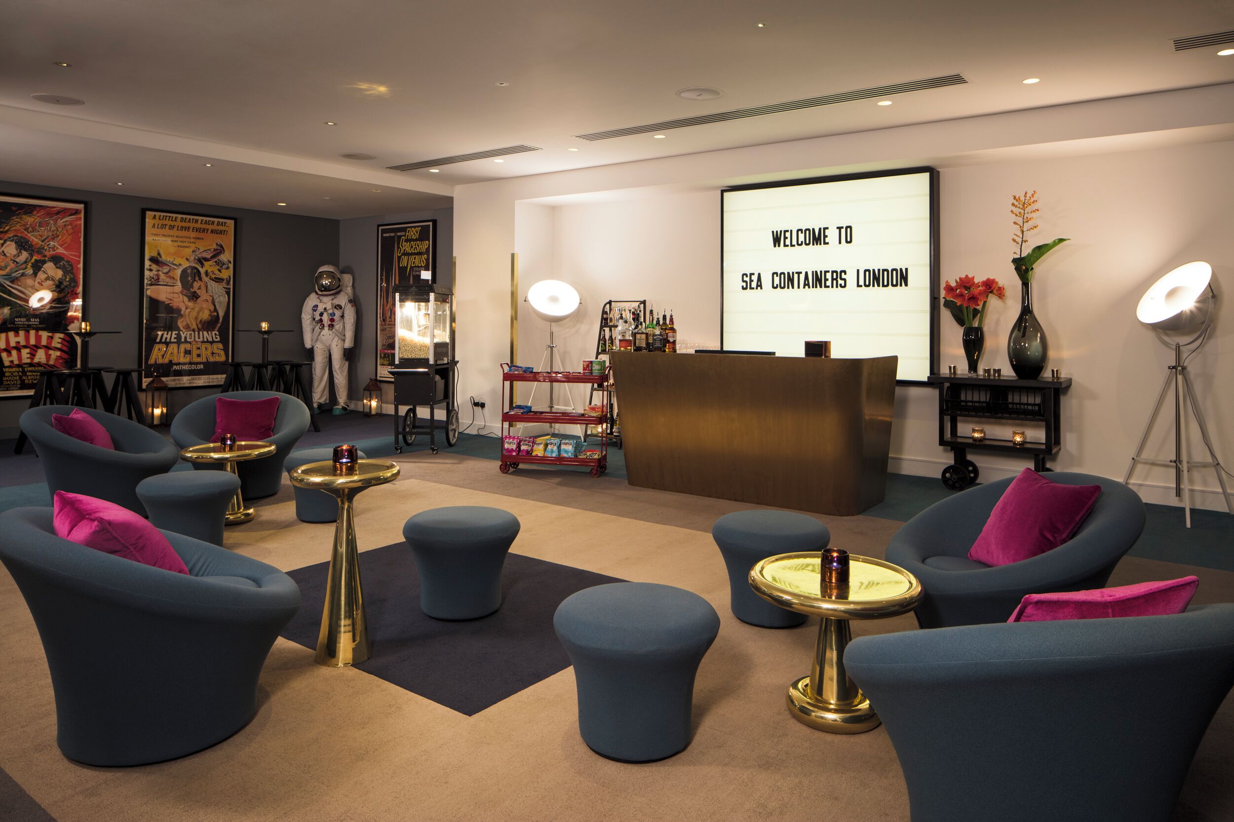 A modern lounge area with blue armchairs, a reception desk, and a screen displaying 'WELCOME TO SEA CONTAINERS LONDON'.