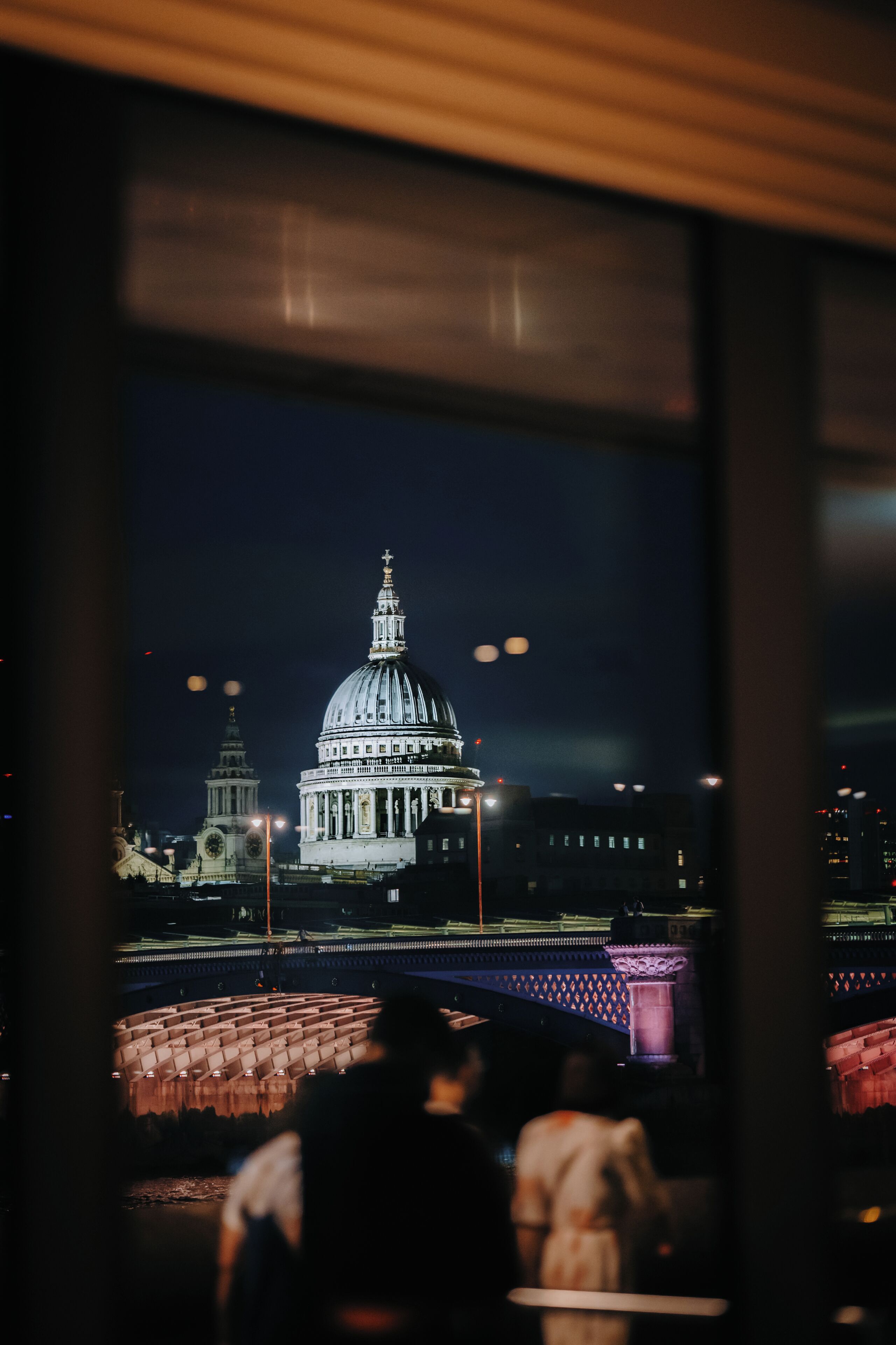 Vista de um grande edifício com cúpula à noite, com uma ponte e estruturas menores em primeiro plano.
