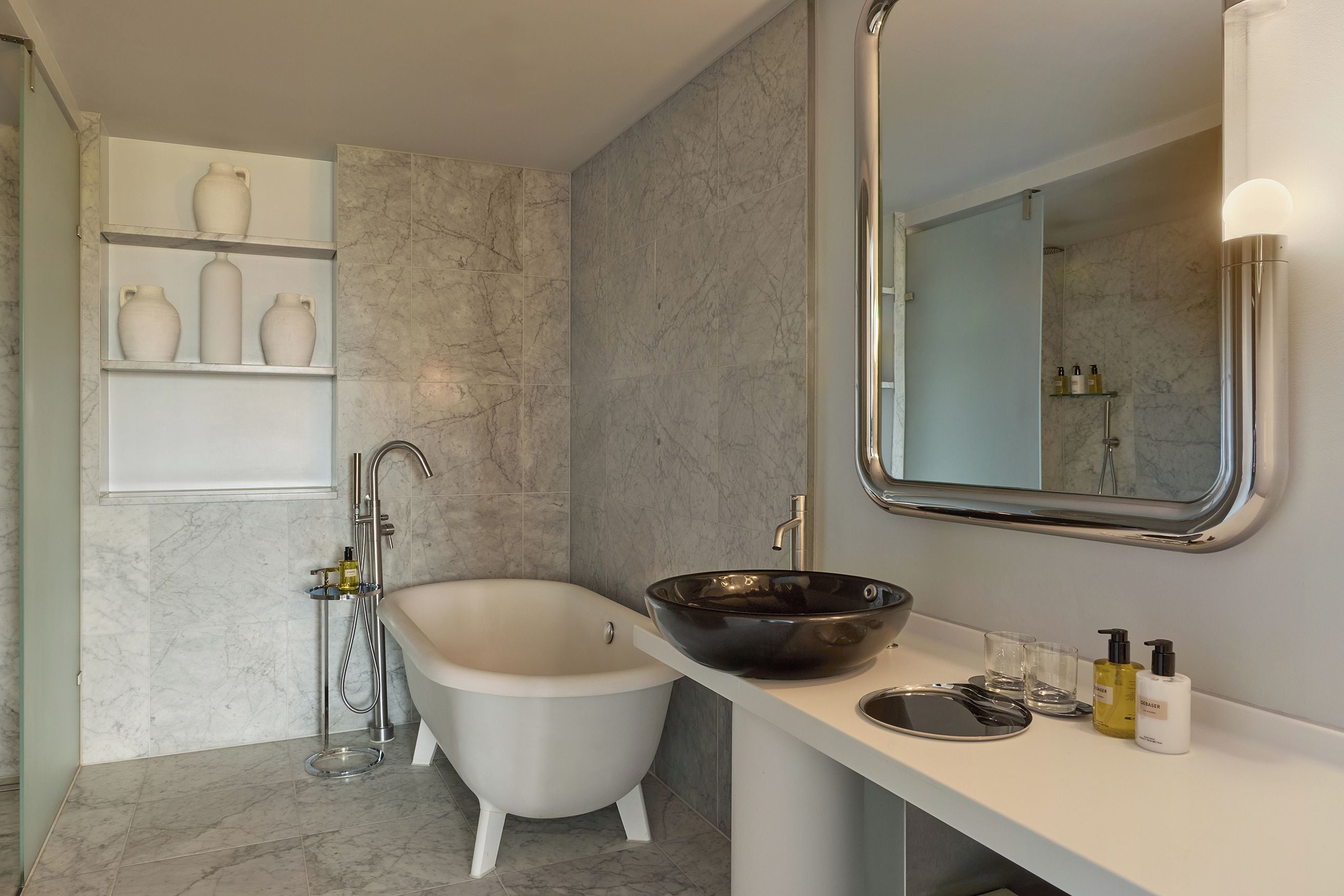 A modern bathroom with a freestanding bathtub, a vessel sink, and a built-in shelf with decorative vases.