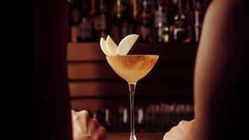 A bar setting with a martini glass on a table, a person partially visible, and a background of shelves with bottles.