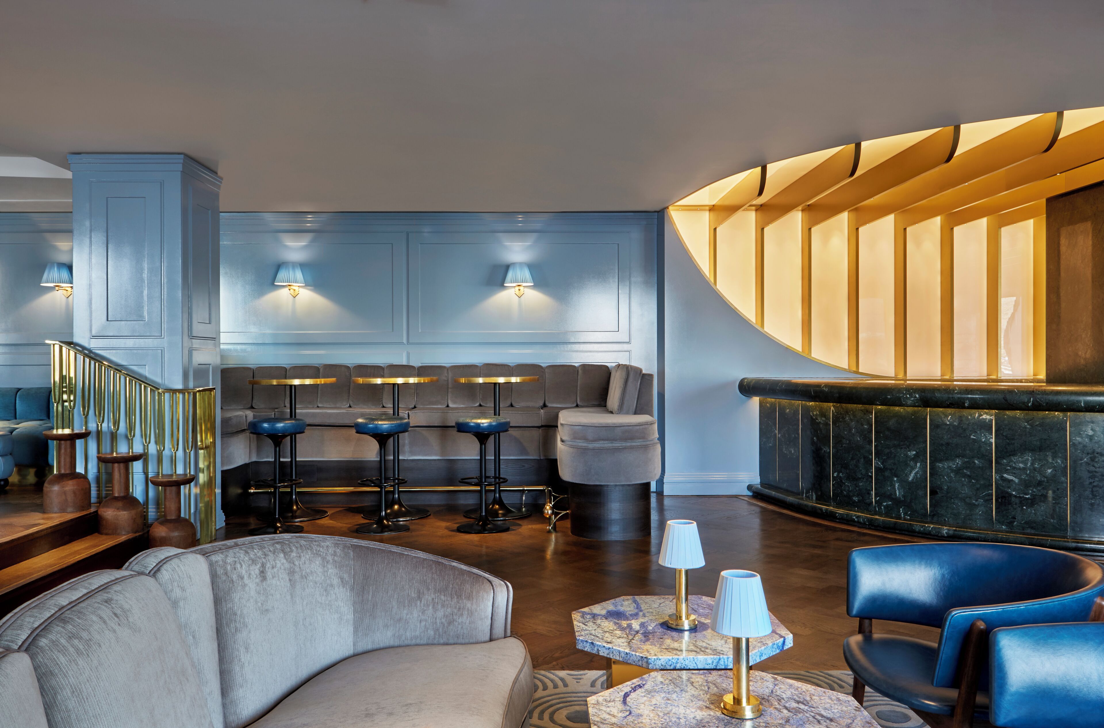 Un hall d’entrée moderne avec un comptoir d’accueil incurvé, un espace détente avec des canapés et des tabourets de bar, et un escalier doté d’une rampe.