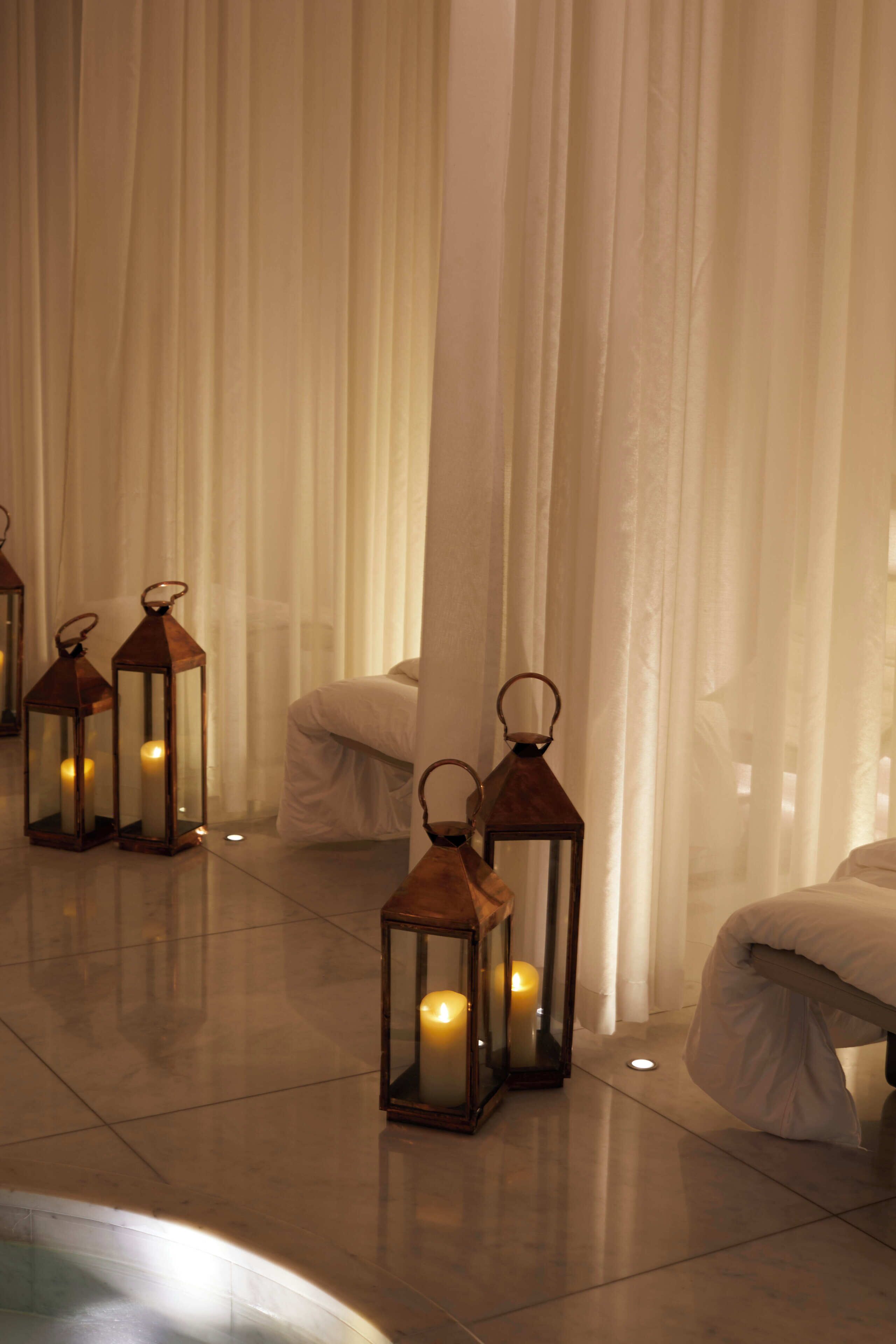 A room with a bed, white curtains, and three lit lanterns.