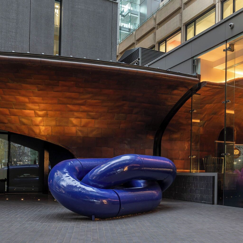 A modern building with a curved facade and a large blue sculpture in front.