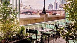 A terrace with green-striped seating, a view of a river, and a bridge in the background. - Sea Containers London (London)