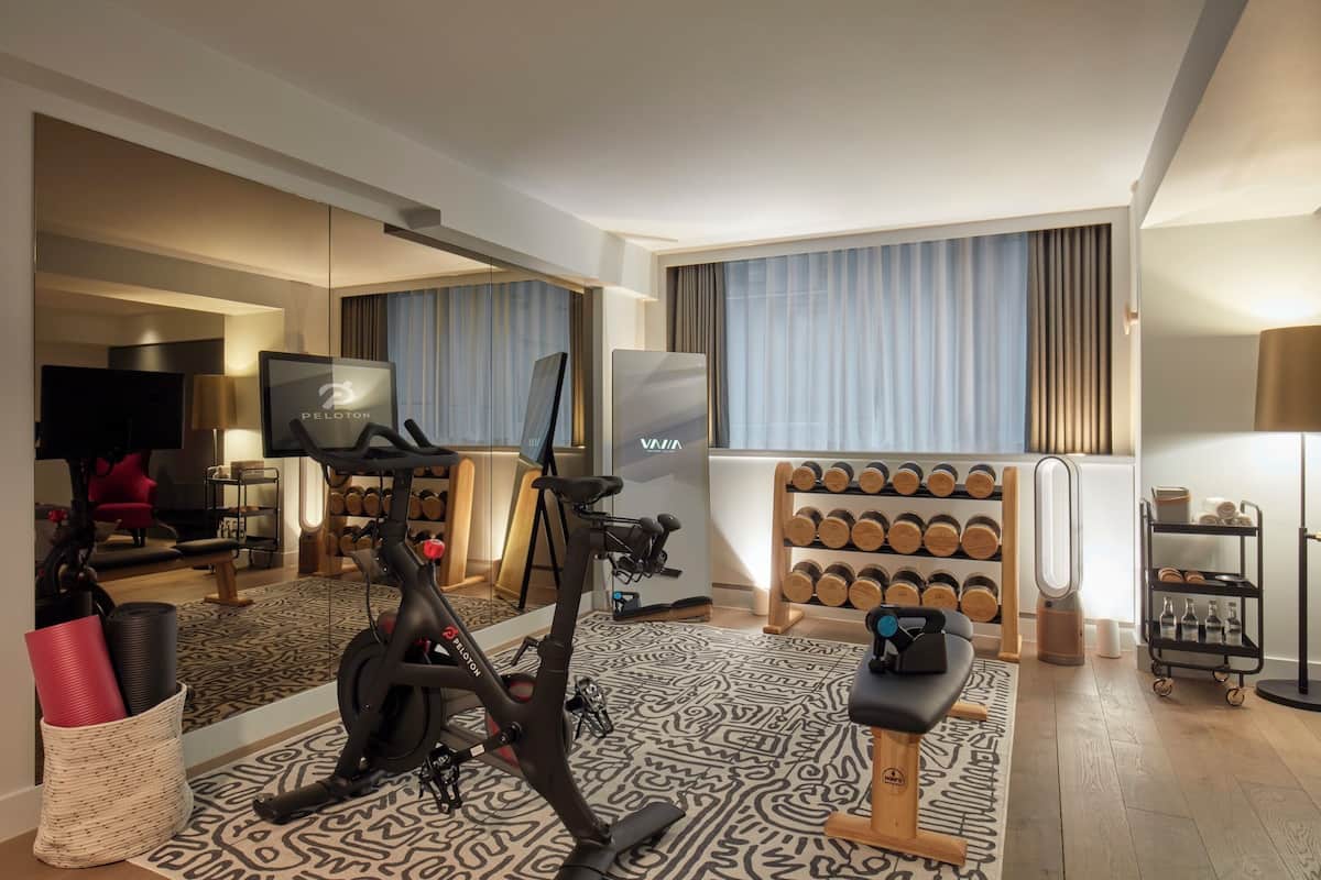 A modern hotel room with a large mirror, exercise equipment, a TV, and a wall-mounted TV.
