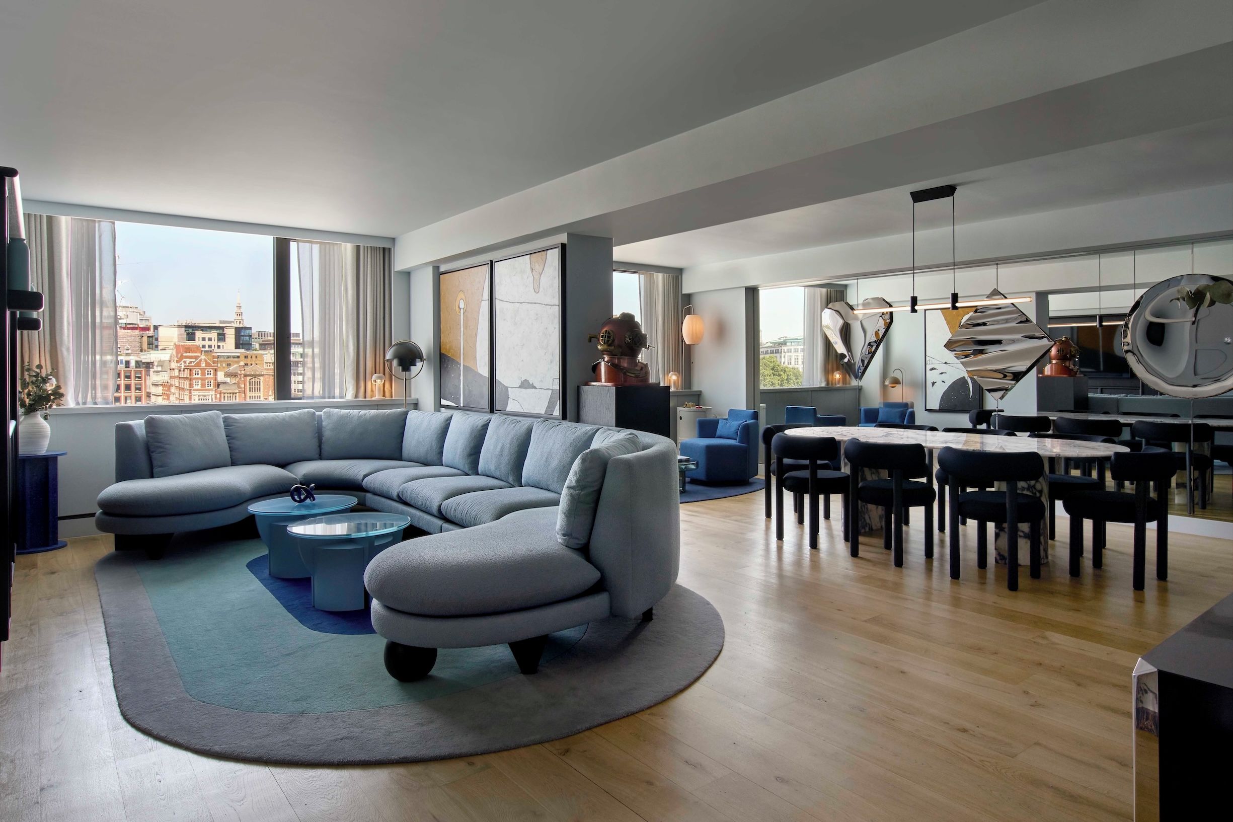 Una sala moderna con un amplio sofá modular, una mesa de centro redonda y una zona de comedor con una mesa de mármol y sillas.