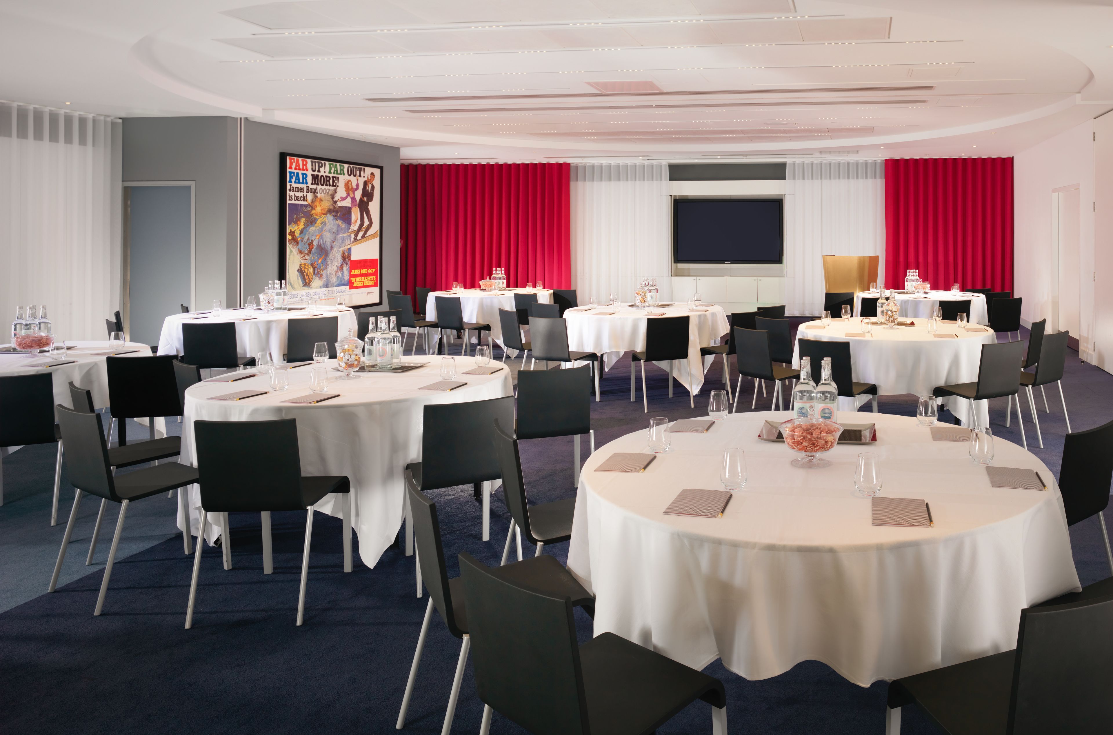 Ein Konferenzraum mit mehreren runden Tischen, schwarzen Stühlen und weißen Tischdecken.