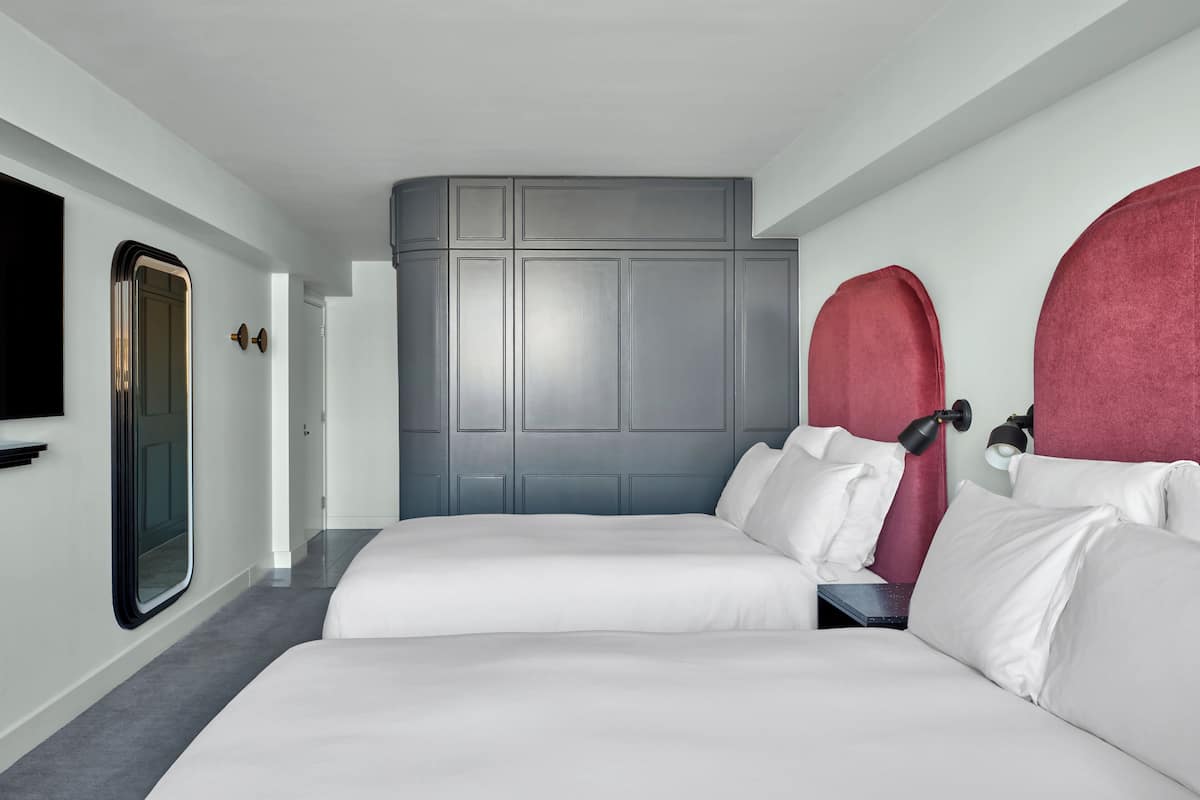 A hotel room with two beds, a grey headboard, a TV, and a red accent wall.
