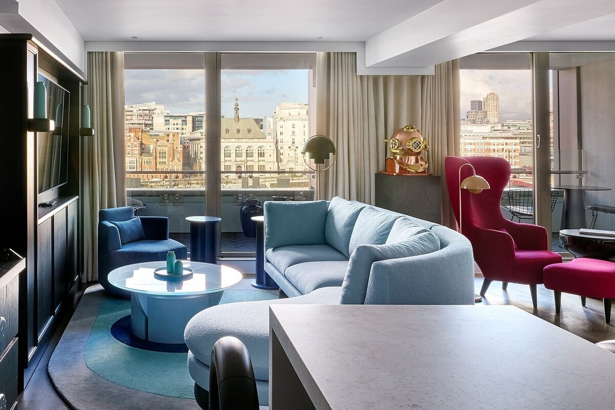 Un salon moderne avec vue sur la ville, comprenant un canapé, des fauteuils, une table basse et une table à manger.