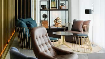 A modern living room with a leather armchair, a sofa, and a round coffee table. There is a glass display case with various items and a floor lamp.
