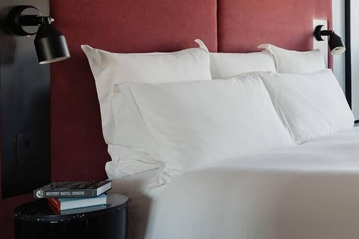 A neatly made bed with white linens and pillows, a black side table with a book, and a red upholstered headboard.