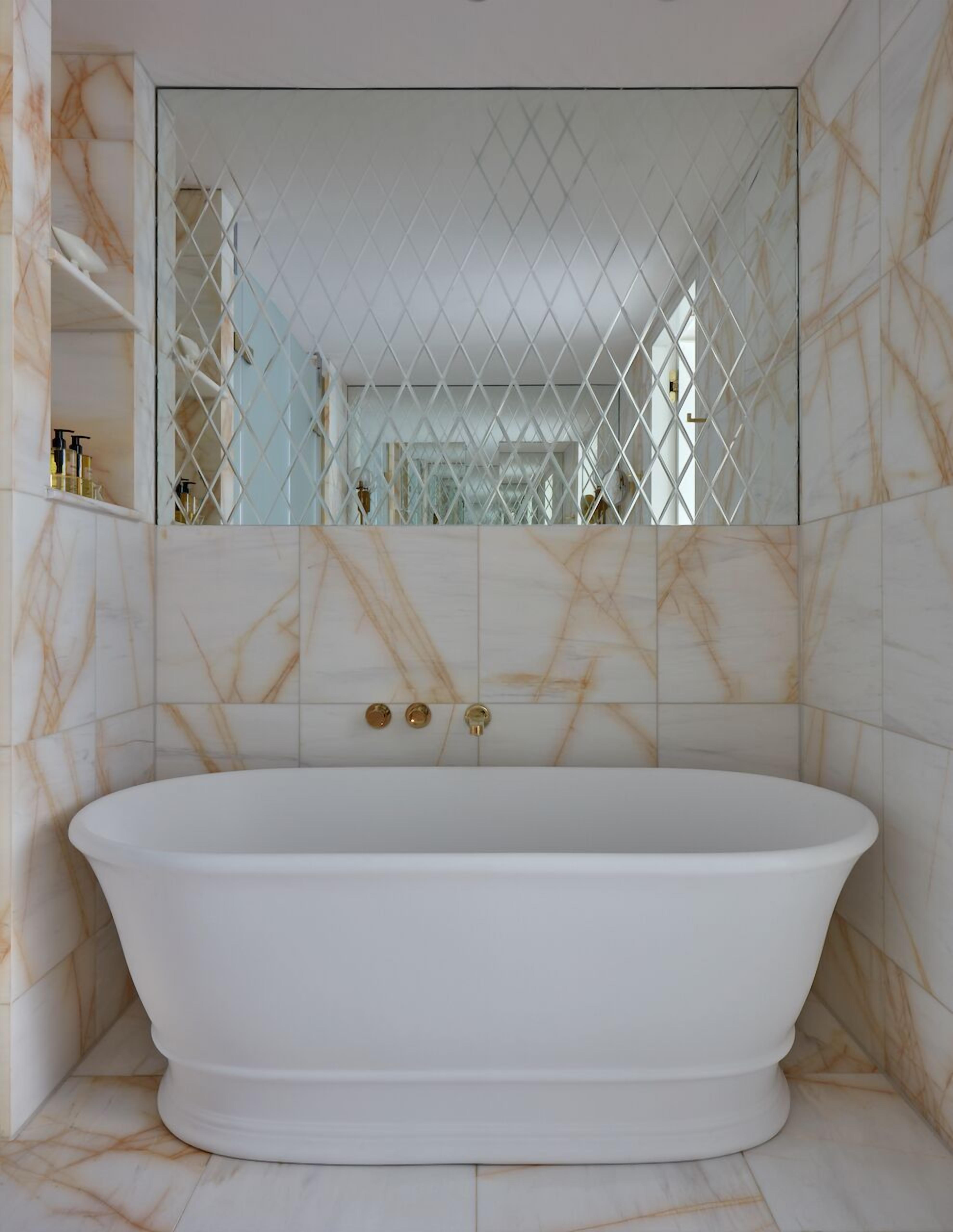 Une baignoire sur pied dans une salle de bain aux murs de marbre et dotée d’un espace clos avec des parois miroir.