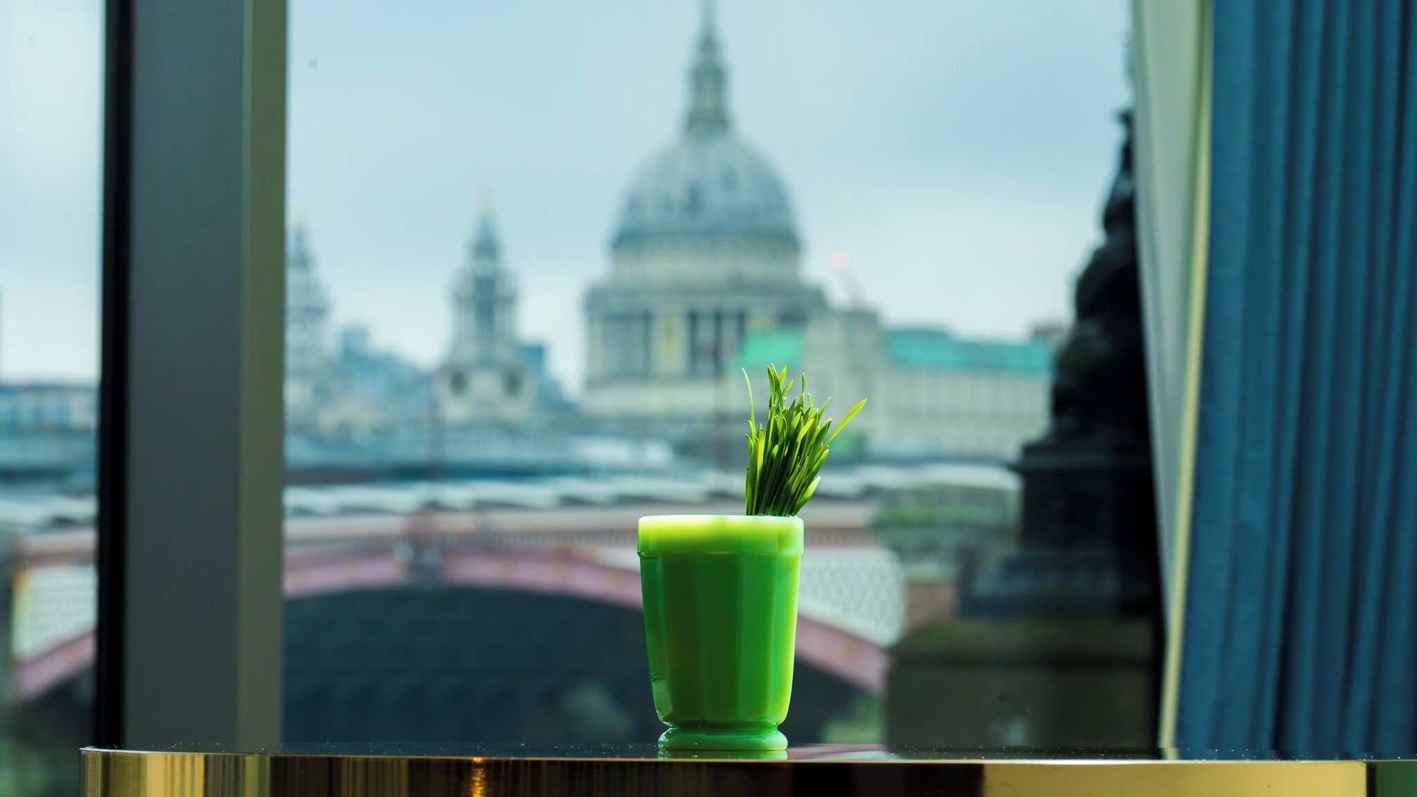 A window with a view of a large dome building, a green vase with a plant, and a reflection of a bridge.
