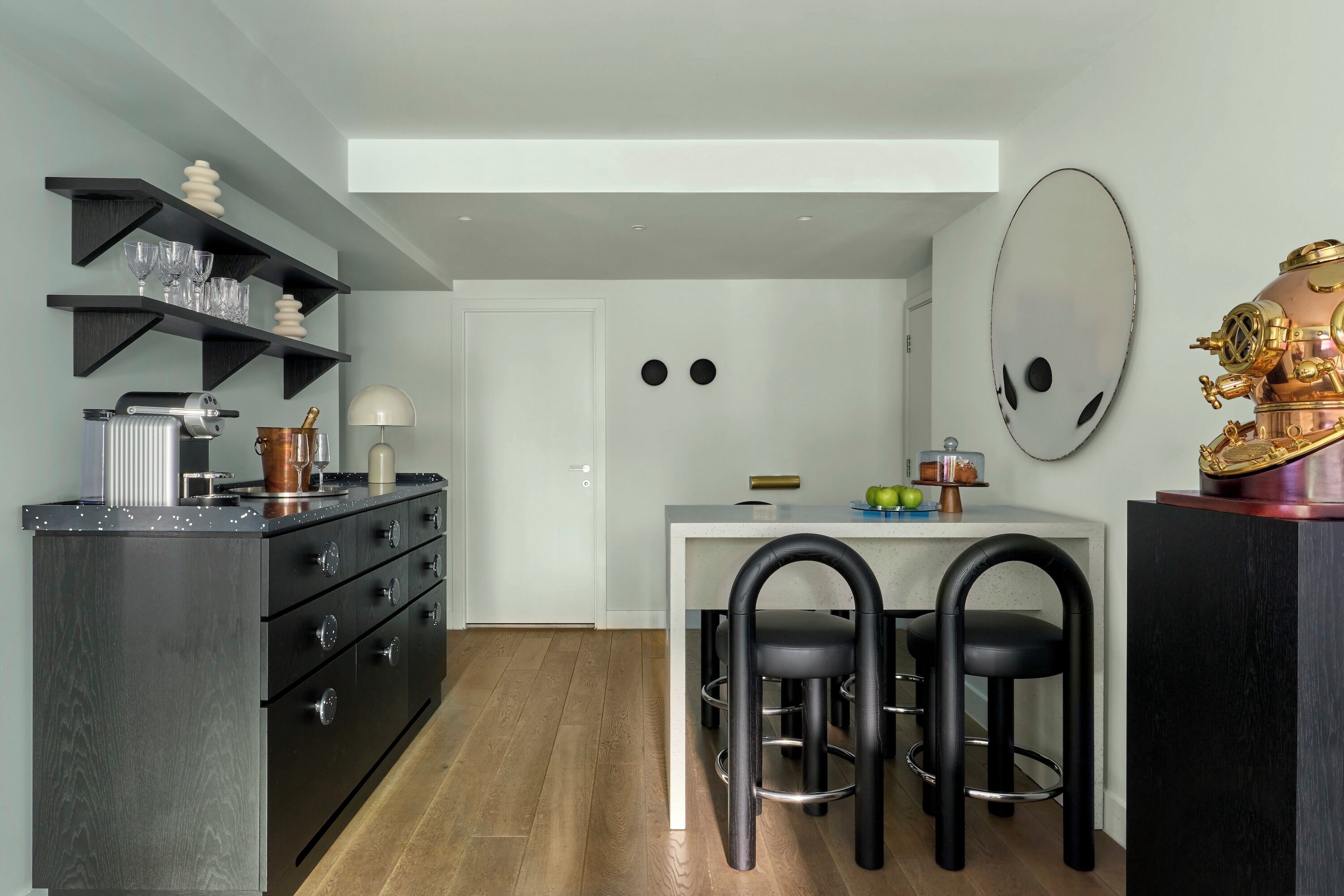Une cuisine compacte dotée d’appareils électroménagers modernes, un coin repas avec des chaises noires et un grand miroir au mur.