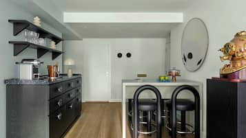 Une cuisine compacte dotée d’appareils électroménagers modernes, un coin repas avec des chaises noires et un grand miroir au mur.