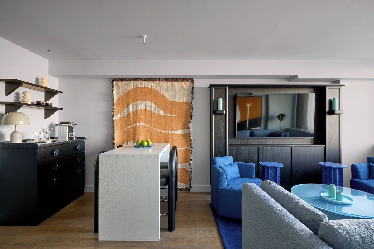 Een moderne woonkamer met een eethoek, een grote flatscreen televisie en blauw meubilair.