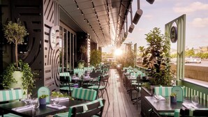 An outdoor restaurant with striped green and white seating, potted plants, and a view of a river. - Sea Containers London (London)