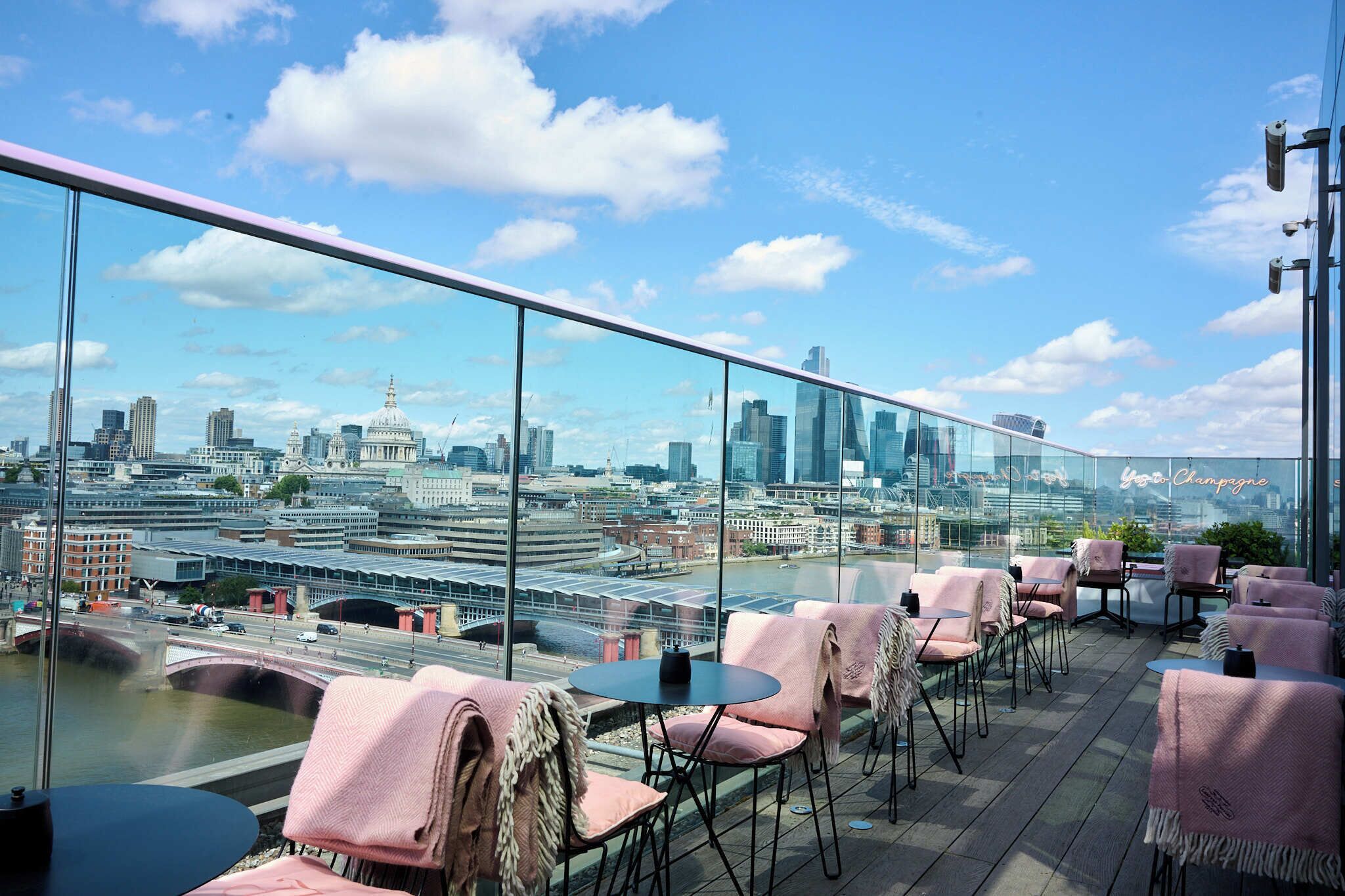 Eine Dachterrasse mit Tischen, Stühlen, einer Glastrennwand und Blick auf die Skyline der Stadt.